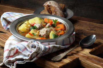 Homemade rustic soup with meatballs, peas, carrots, potatoes, onions, garlic, chili and parsley