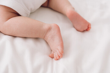 Fototapeta na wymiar legs of newborn baby on white sheet close-up, baby learns to crawl