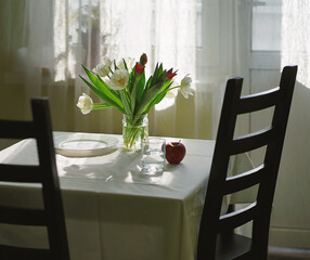 A bouquet of tulips on the table, white dishes, the table is covered with a white tablecloth.