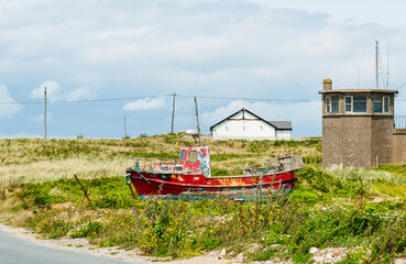Fototapeta na wymiar Red fisherman boat abandoned by a road in a meadow. Forgotten or forsaken fishing trawler in the grass. Sadness and decay concept. Fishing dying business or industry. Kilmore Quay, Wexford, Ireland