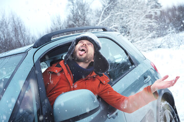 Happy positive man driver leaning out car window and catching snowflakes by mouth enjoying snowfall...