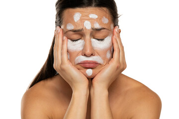 Unhappy sad woman posing with face cream on a white