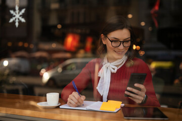 Stylish young woman drinking coffee at cafe. Beautiful girl using the phone while enjoy in fresh coffee.