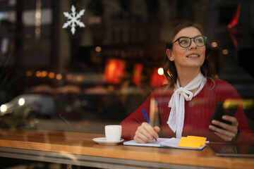 Stylish young woman drinking coffee at cafe. Beautiful girl using the phone while enjoy in fresh coffee.
