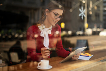 Happy woman using credit card to shopping online with tablet. Beautiful young woman drinking coffee in cafe..