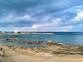 Rocky shore with sand, sandy beach, the temple of St. Nicholas the Wonderworker against the backdrop of a dramatic sky.