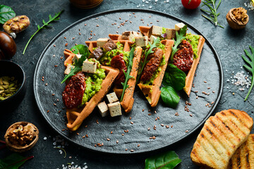 Waffle sandwiches with avocado pate, sun-dried tomatoes and tofu cheese. The concept of dietary nutrition. On a stone background.