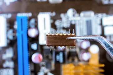 Microcircuit in tweezers on the background of the motherboard