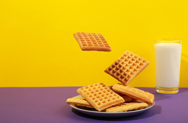 Belgian waffles flying in air on colorful background. Waffles in plate with milk and honey. Creative food concept.