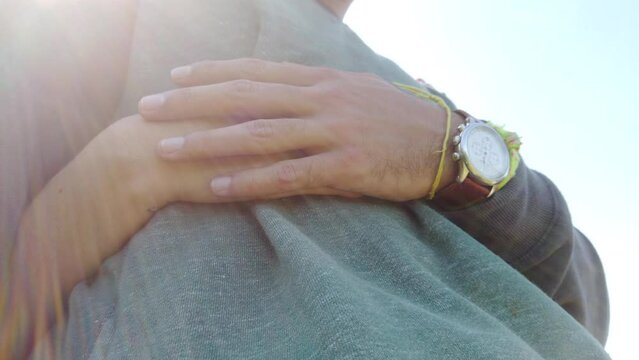 Young man's hand caressing woman's hand that is embrace him down sunlight.