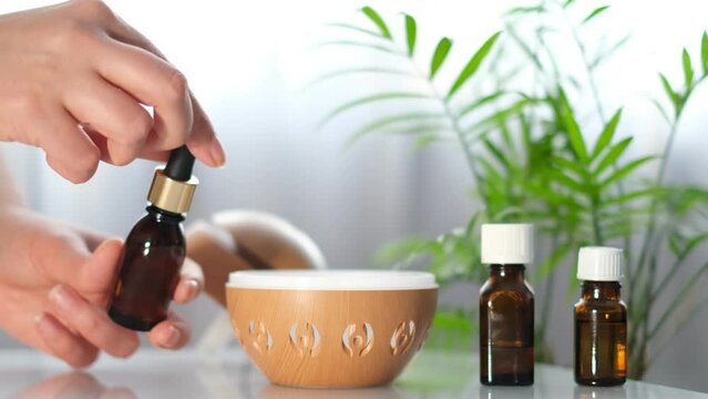 Modern aroma oil diffuser on the white table. Spa concept for body and health care. female is adding essential oil to an aroma diffuser.