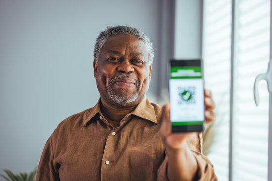 Senior man showing International Certificate of Covid-19 vaccination. African American senior man shows vaccine passport on mobile phone to validate travel permission by the digital document