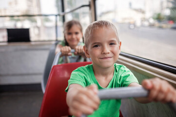 Girl and boy riding together in empty tram and looking at camera with smile, city tramway. Train lines are outside the glass. Cheap and attractive form of public transportation