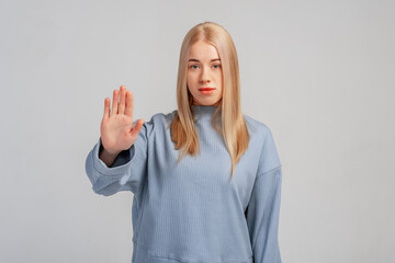 Serious blonde girl showing stop sign and frowning displeased, telling no, refusing something,...