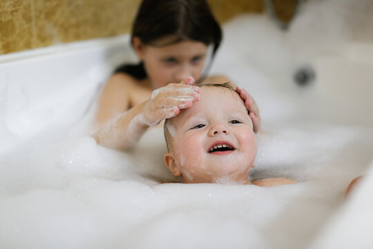 Cute sibling children bathe in a bubble bath together. Children in the bathroom. The concept of hygiene and education.