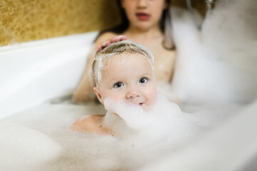 Cute sibling children bathe in a bubble bath together. Children in the bathroom. The concept of hygiene and education.