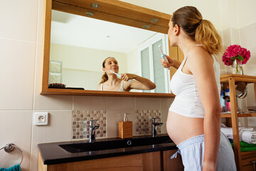 Pregnant woman brush teeth standing at bathroom