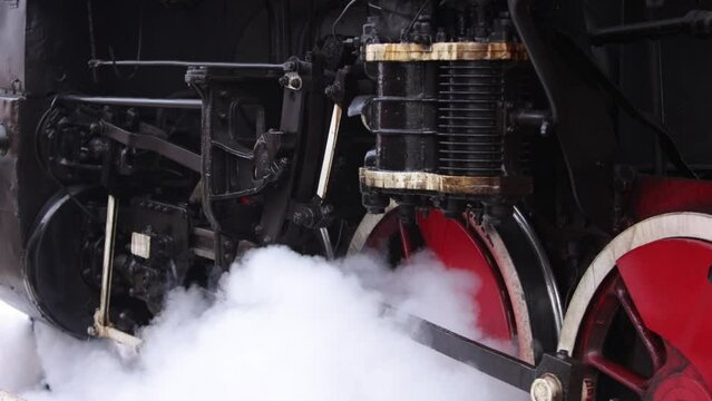 Old wheels and parts of a steam engine close-up. Soviet locomotive stands on the platform of station. Vintage trains with steam on move.