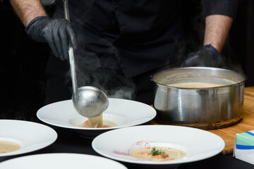 Chief cooking fish cream soup with salmon, cheese and herbs in white soup bowls