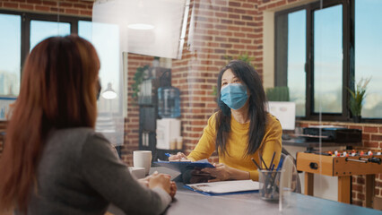 Women meeting at job interview appointment during covid 19 pandemic. Business employee talking to candidate about job information and recruitment, wearing face mask in company office.