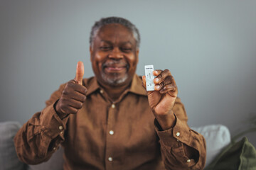 A senior man in his 60s taking a Covid-19 lateral flow self-test at home. The man is of African American ethnicity, and he is wearing a shirt. Room for copy space.