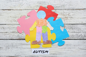 Colorful human figure and puzzle pieces with word AUTISM on white wooden background