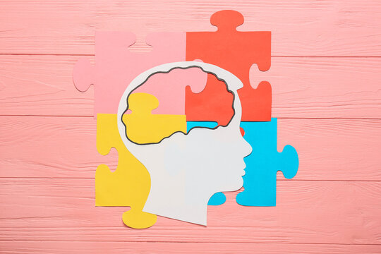 Paper human head and colorful puzzle pieces on color wooden background. Concept of autistic disorder
