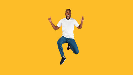 Fototapeta na wymiar Excited African Man Gesturing Thumbs Up Jumping Over Yellow Background