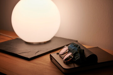 Sonnenbrille und Brillenputztuch liegen auf einem Notizbuch vor einer hell leuchtenden Kugellampe...