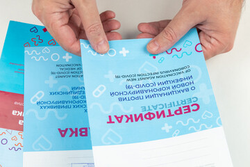 Male hands hold Russian certificates of vaccination against coronavirus infection COVID-19, close-up. Official state Russian documents on vaccinations. Cyrillic inscription CERTIFICATE and MEMO
