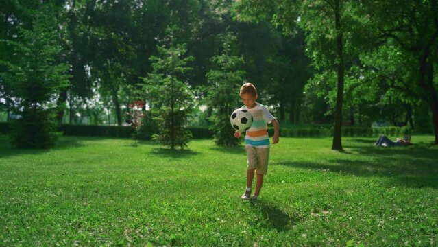 Little boy kicking soccer ball. Focused child practicing in summer park alone.