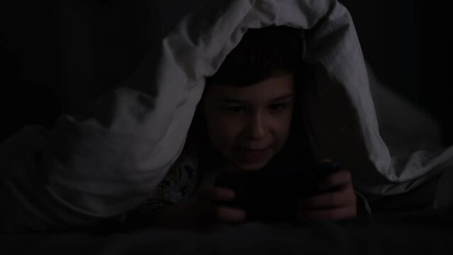 boy playing the phone in the dark. Prolonged telephone play negatively affects eye sight and health in young children. Dependency on a cell phone.