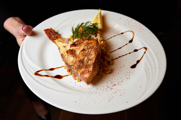 Waiter holding a plate of baked fish with garnish