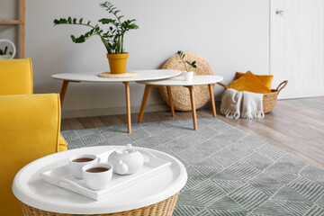 Tray with teapot and cups on table in stylish living room