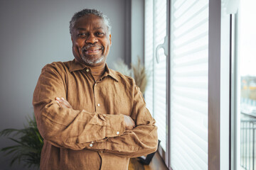 Portrait of smiling senior african american man at home near window. Portrait Of Happy Senior Man...