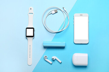 Power bank with USB cable, earphones, smartwatch and mobile phone on blue background