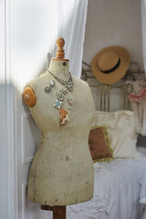 An old vintage mannequin with brooches. In the background is a bed and a hat. Vintage interior.
