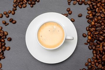 white cup with espresso coffee on a saucer with coffee beans on a dark background