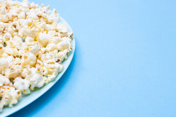 Popcorn and place for text. Popcorn on a turquoise plate for watching a movie. Blue background. Copy space. Flat lay. Top view. Quick and tasty snack
