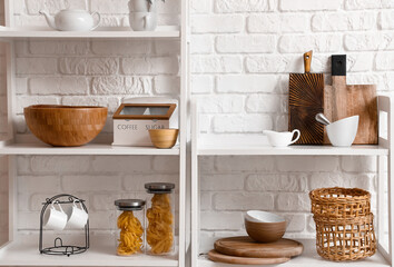 Naklejka na ściany i meble Modern shelf units with kitchenware near white brick wall