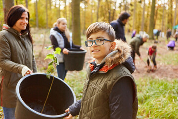 Kleiner Junge hilft Familie beim Baum pflanzen im Wald