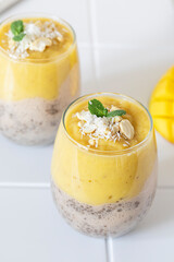 Delicious mango and chia pudding in a glass on the white ceramic tile table close up. Healthy morning breakfast concept	