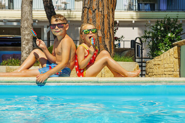 Happy siblings on vacation eating ice cream at swimming pool