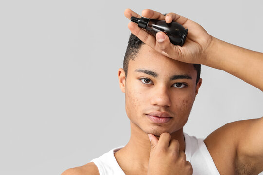 Young African-American guy with serum for skin care on grey background