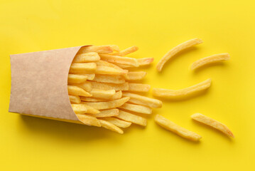 Paper box with tasty french fries on yellow background