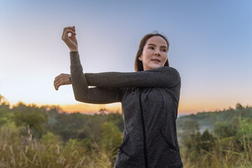  Beautiful young Asian woman in warm up jacket stretching her arms up during her break from her...