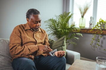 Active senior man measuring blood pressure with sphygmomanometer in bedroom. An older African...