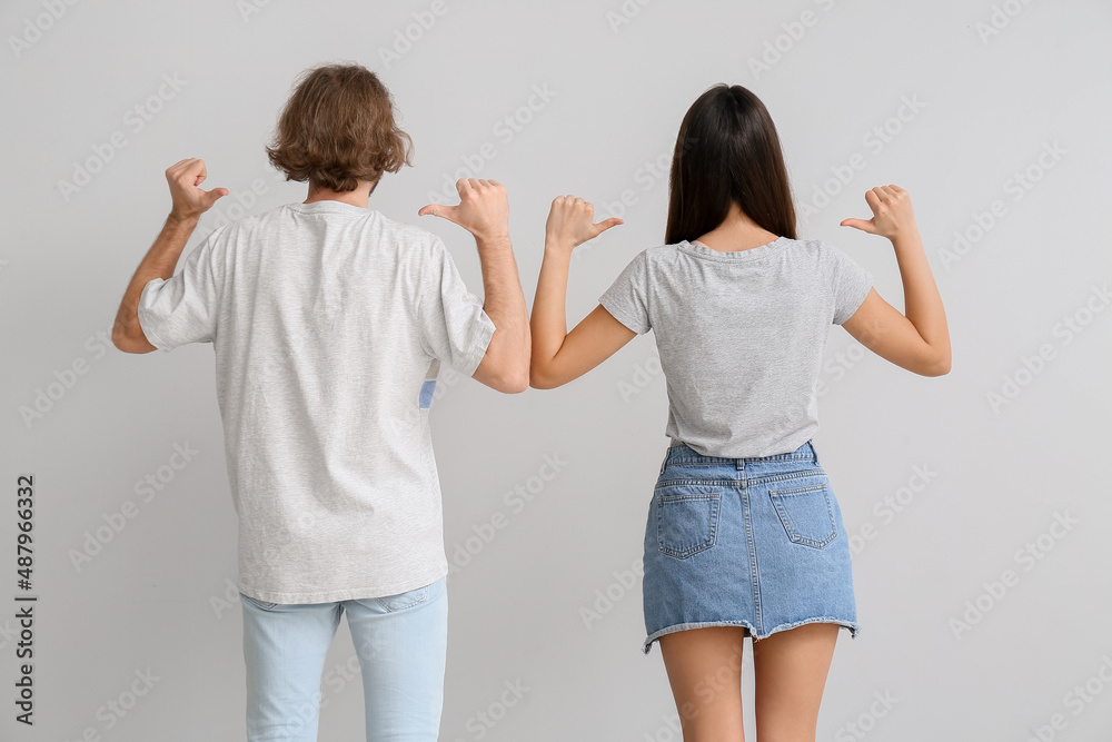 Sticker young couple in stylish t-shirts on light background, back view