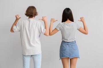 Young couple in stylish t-shirts on light background, back view