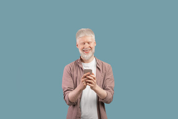 Online life. Happy albino man using smartphone, chatting online, browsing social media over turquoise studio background